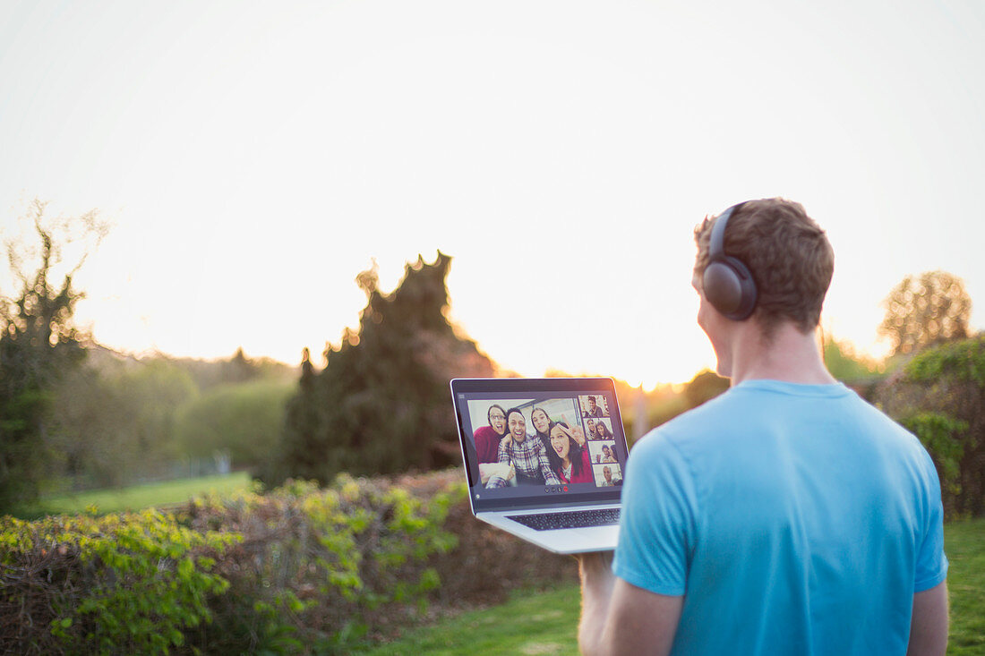 Man with headphones video chatting with friends in garden