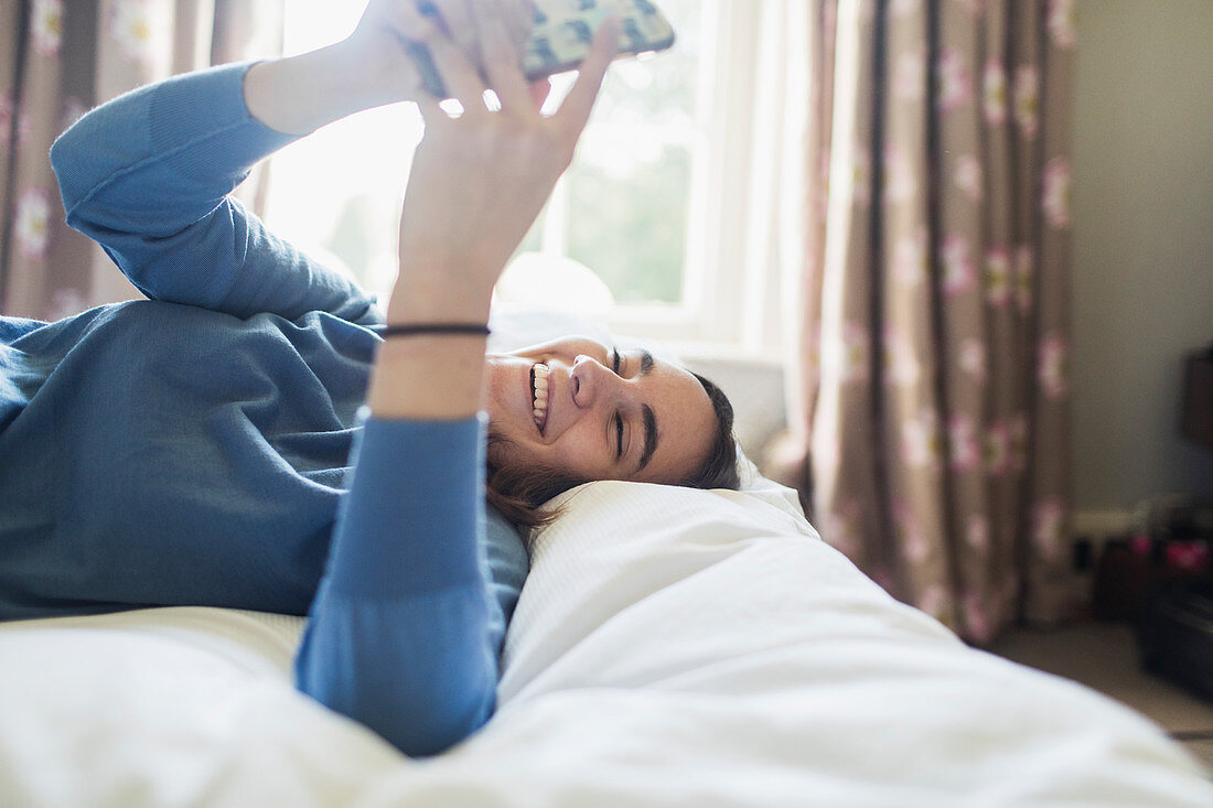 Happy teenage girl using smart phone on bed