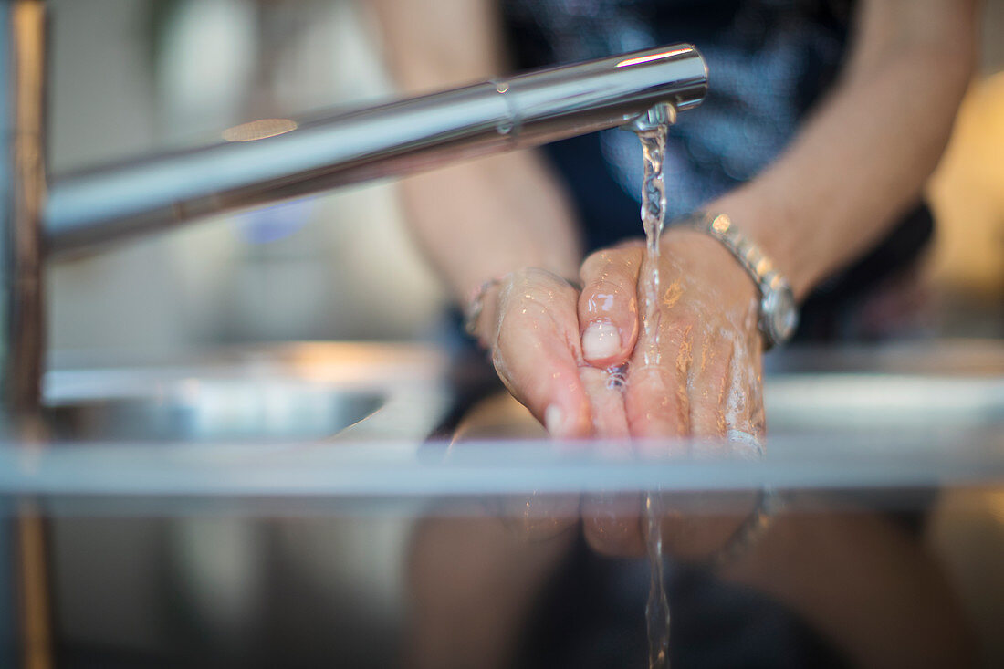 Close up woman washing hands at kitchen sink