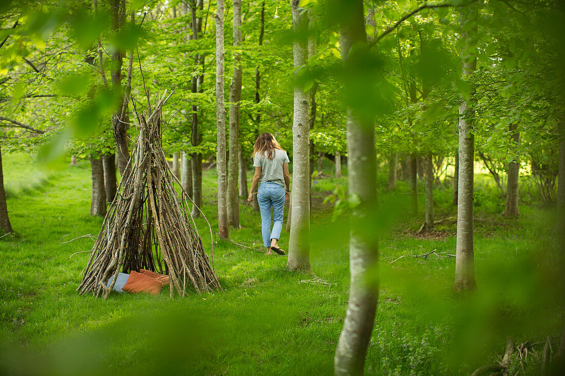 Woman near branch teepee in woodland
