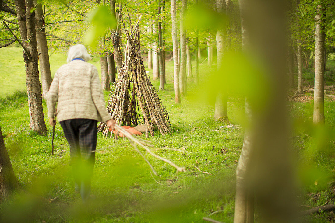 Senior woman making branch teepee in woodland