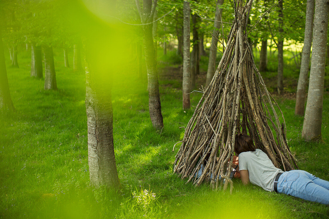 Woman relaxing in branch teepee in woodland