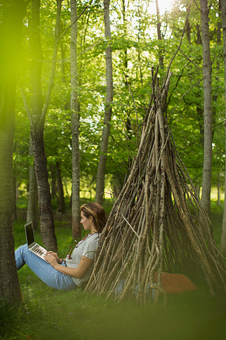 Woman using laptop at branch teepee in woodland