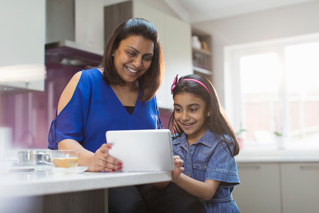 Happy mother and daughter using digital tablet in kitchen