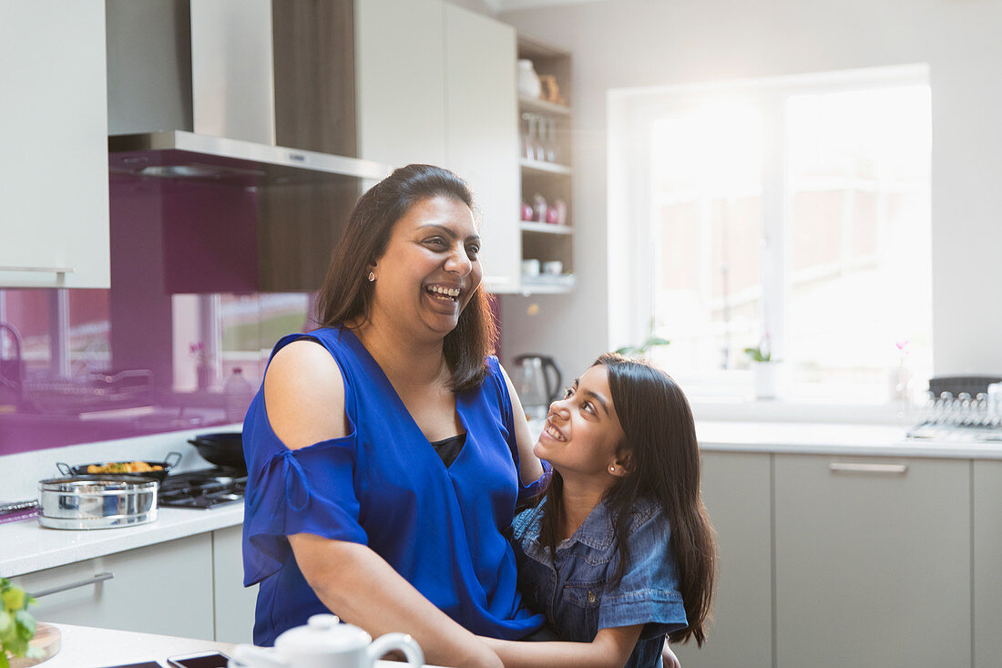 Happy mother and daughter hugging in kitchen