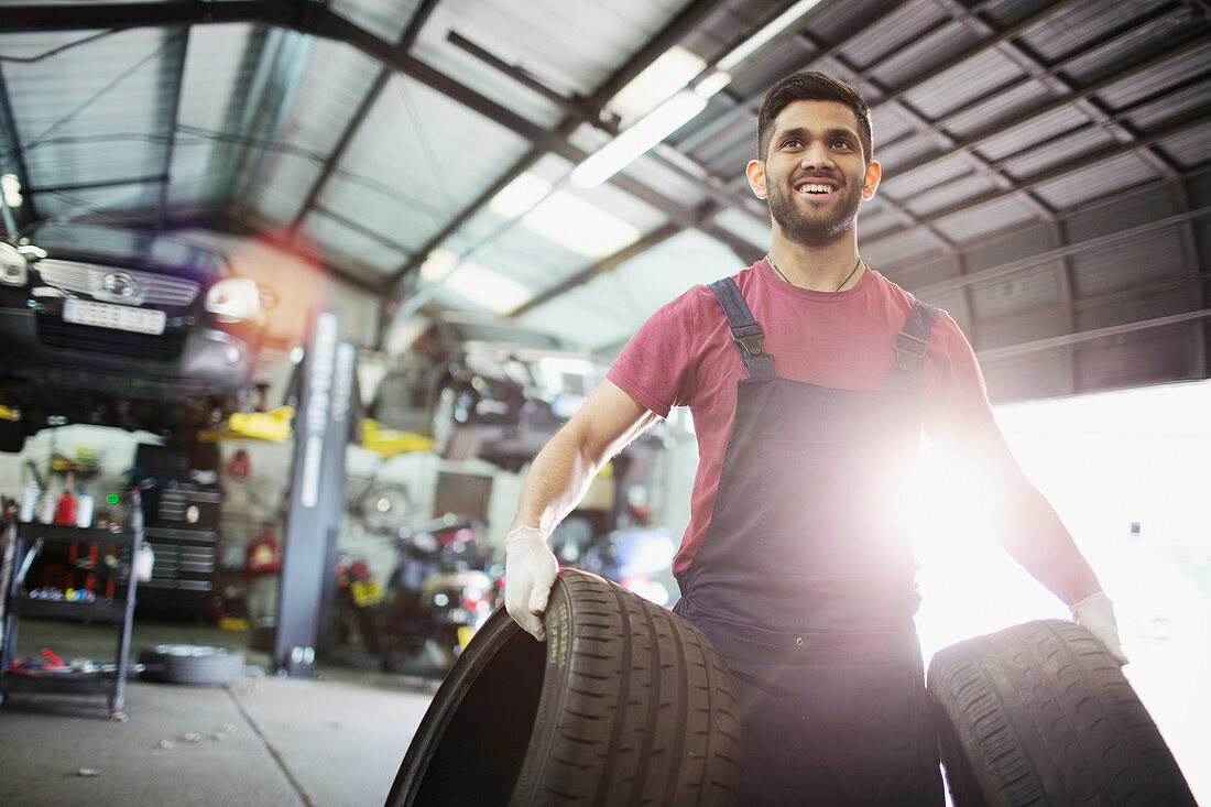Portrait smiling male mechanic carrying tires