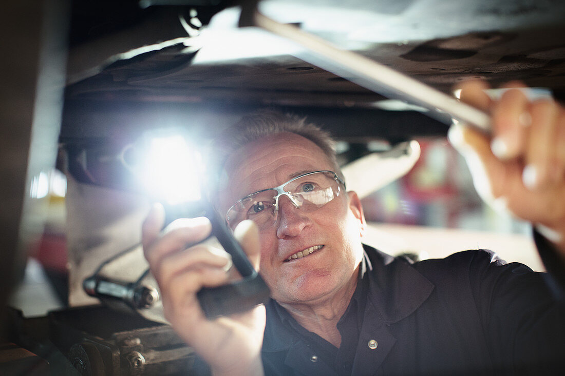 Male mechanic with flashlight working under car