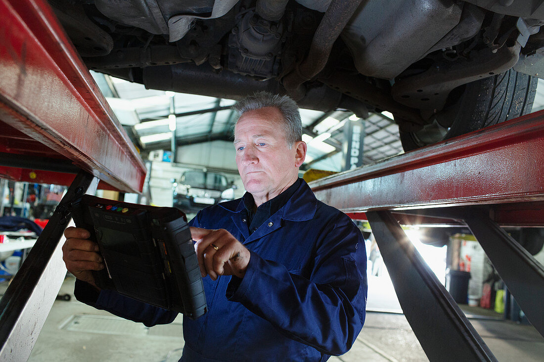 Male mechanic using diagnostic equipment under car