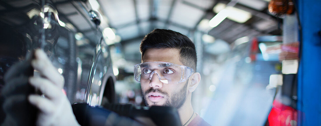 Focused male mechanic examining car