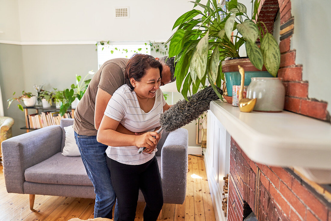 Mature couple with duster dusting living room