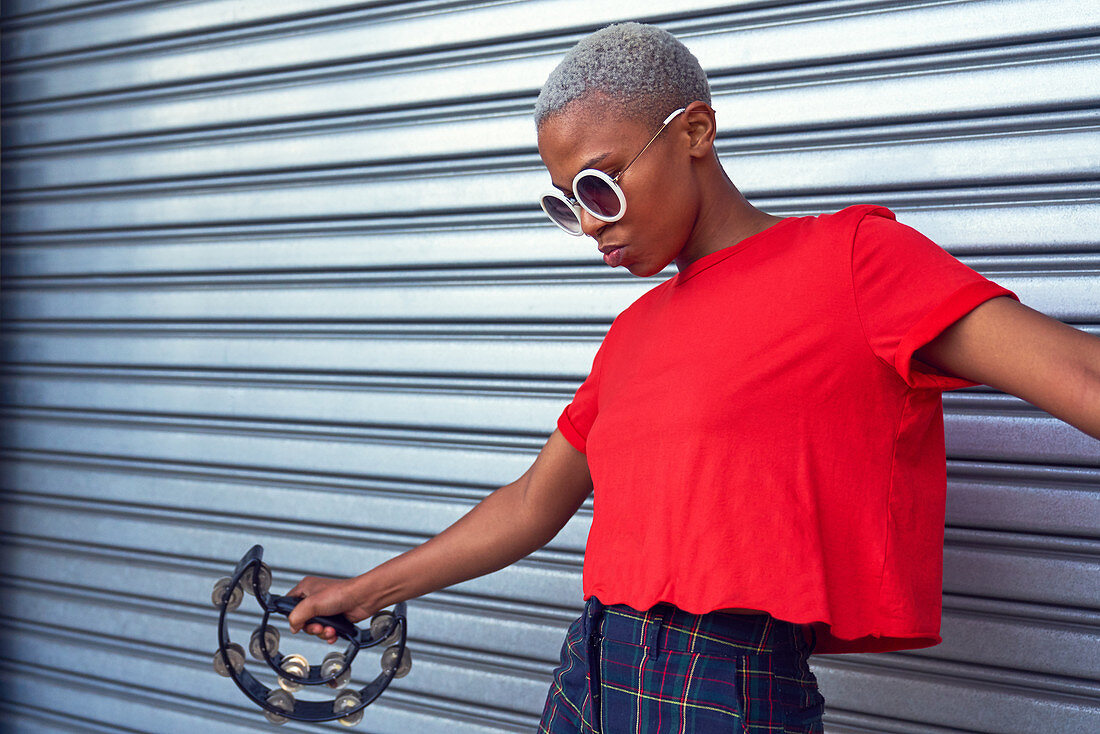 Cool young woman playing tambourine outside garage