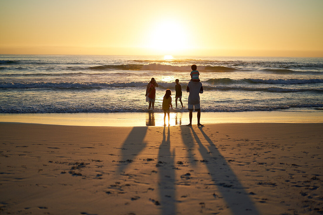 Family wading in summer ocean surf at sunset