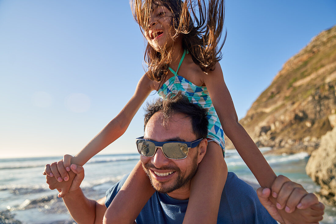 Father carrying daughter on shoulders on beach