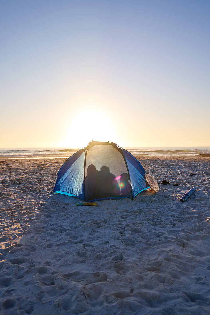 Silhouette family inside tent on sunset beach