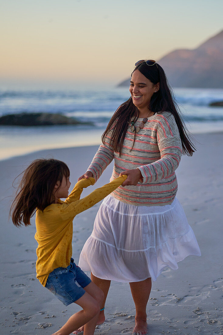 Playful mother and daughter dancing on beach
