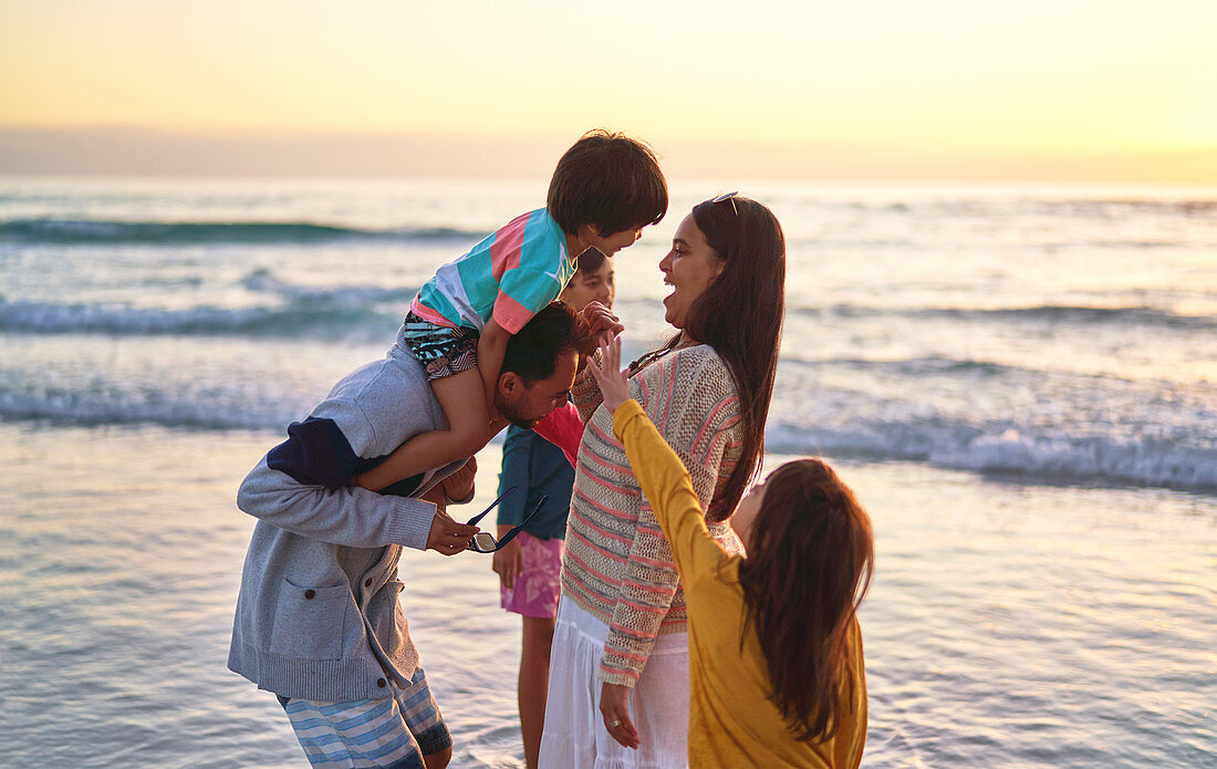 Happy family wading in ocean surf on sunset beach