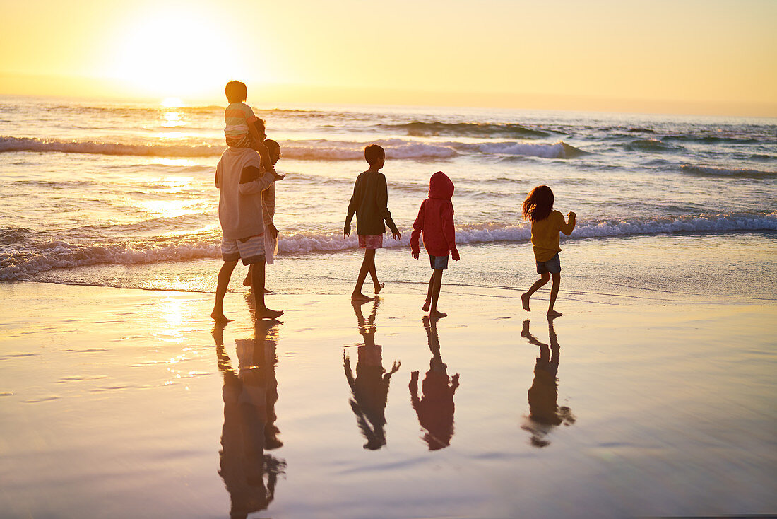 Family walking in ocean surf on beach at sunset