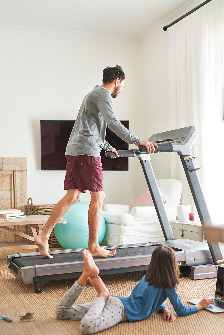 Daughter using laptop next to father on treadmill