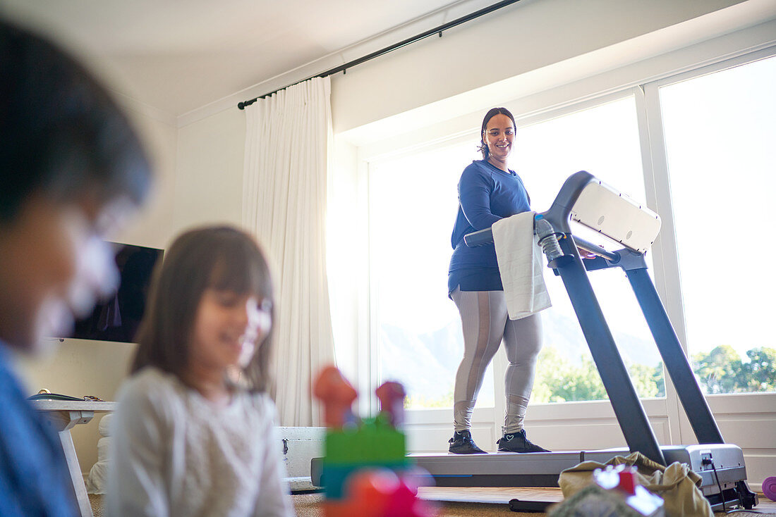 Mother exercising on treadmill and watching kids