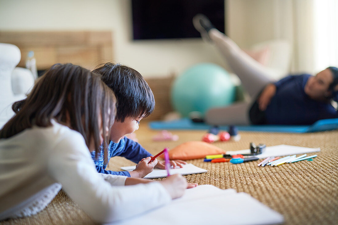 Kids colouring on floor near mom exercising