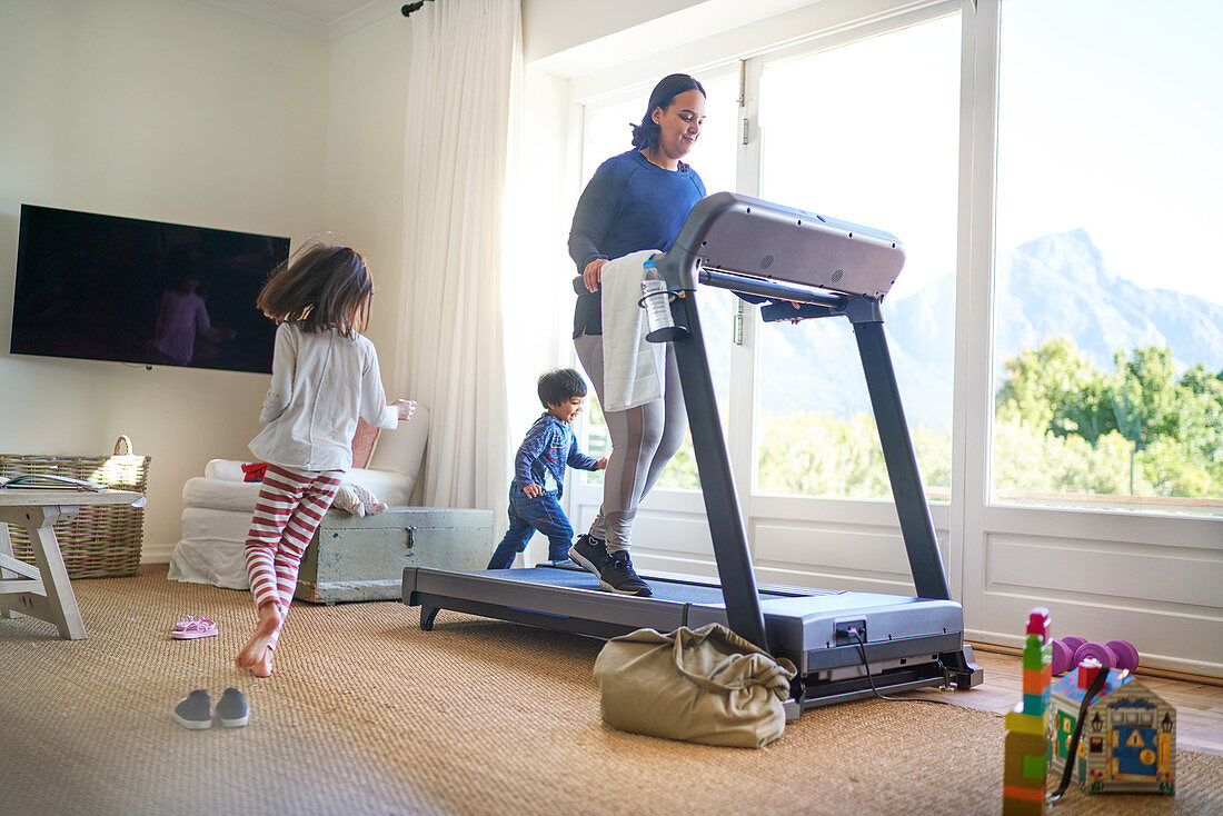 Kids running around mother exercising on treadmill