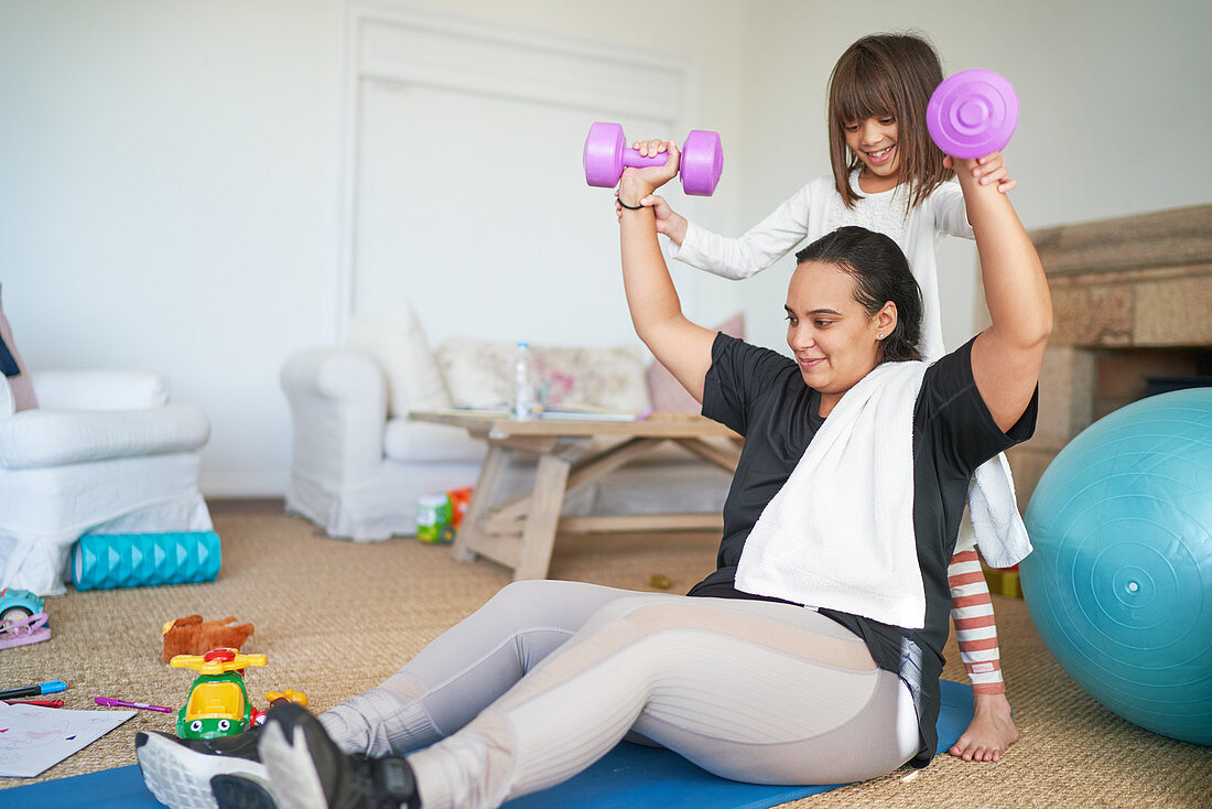 Daughter helping mother exercising with dumbbells