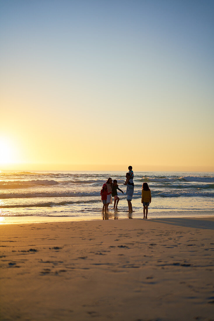 Family wading in ocean surf on beach at sunset