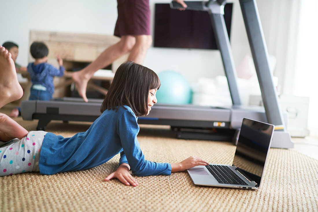 Girl using laptop, father on treadmill