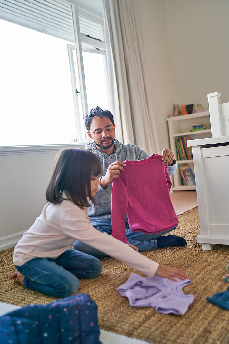 Father helping daughter fold clothes in bedroom
