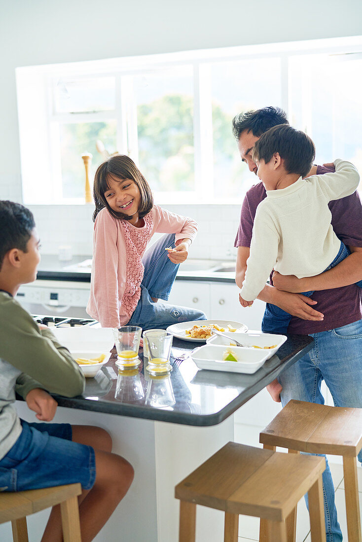Father and kids eating takeout food in kitchen
