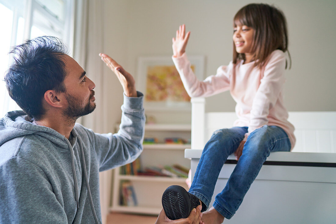 Father and daughter high-fiving in bedroom
