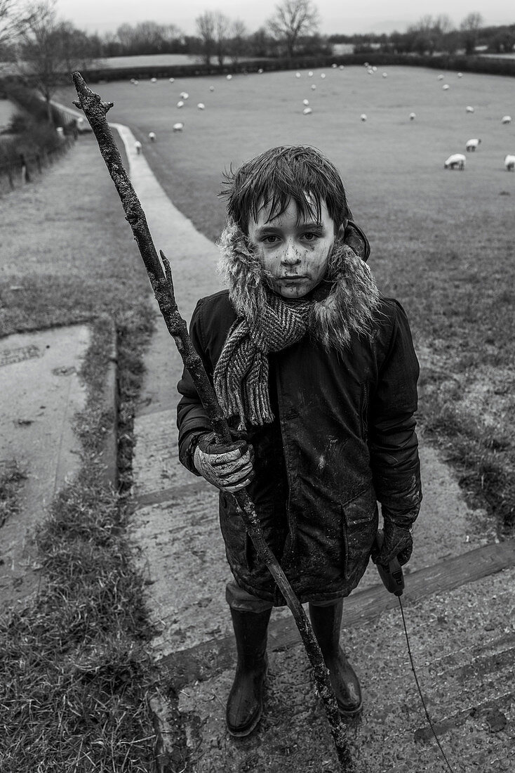 Portrait muddy boy with stick in rural field