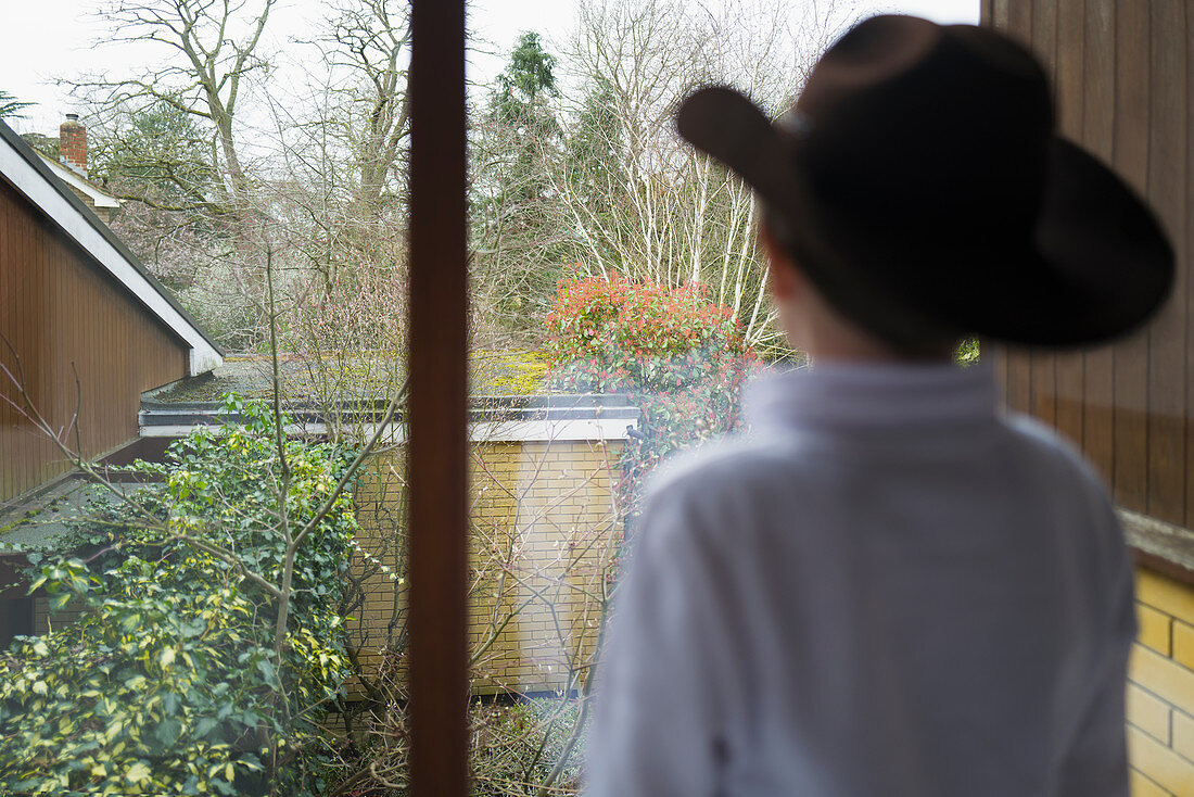 Boy in cowboy hat looking out home window