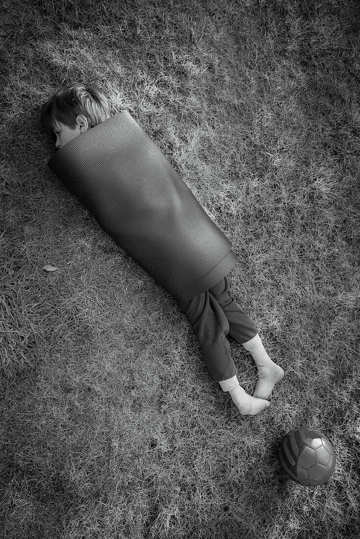 Boy wrapped in yoga mat in grass