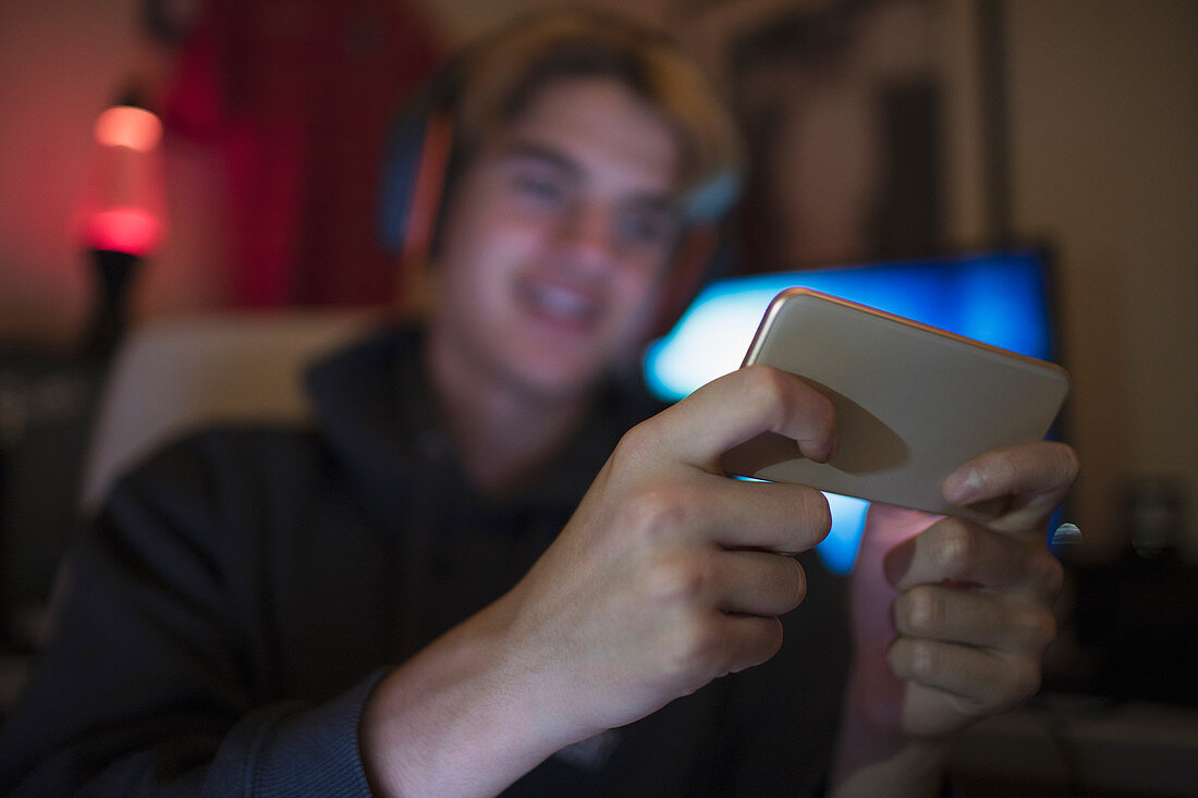 Teenage boy using smart phone in dark bedroom