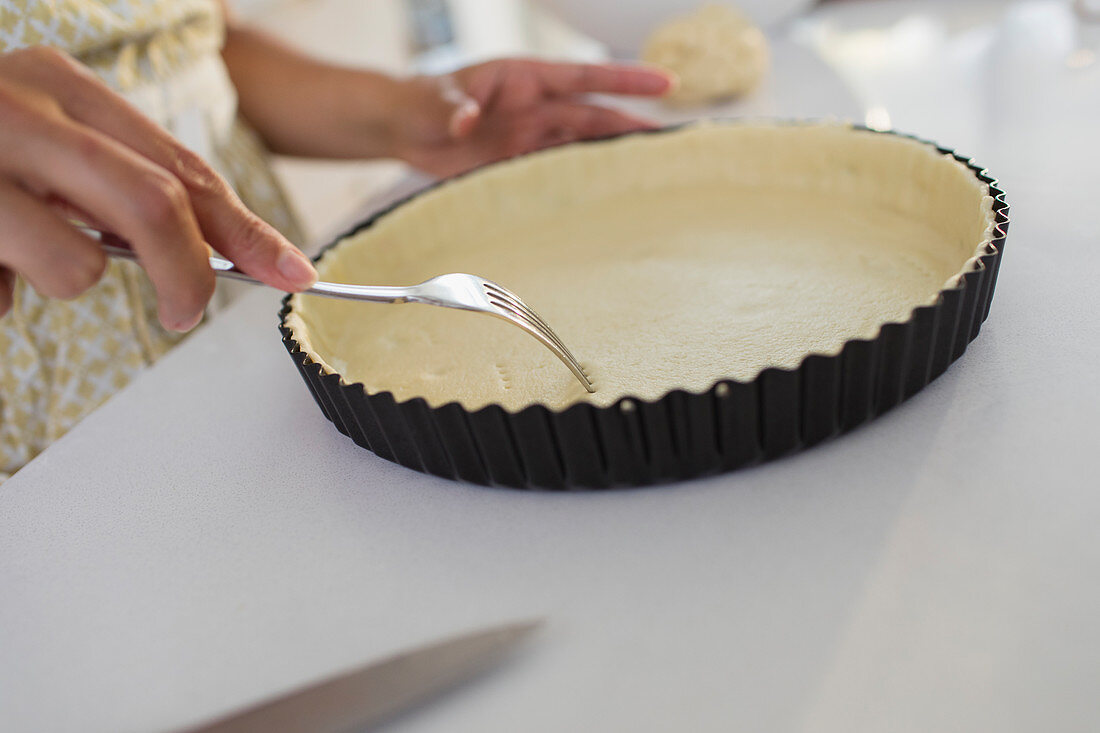 Woman baking poking holes into pie crust with fork