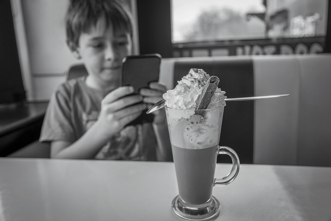 Boy with smart phone enjoying milkshake in diner