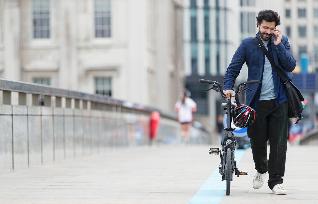 Businessman with smart phone walking bicycle
