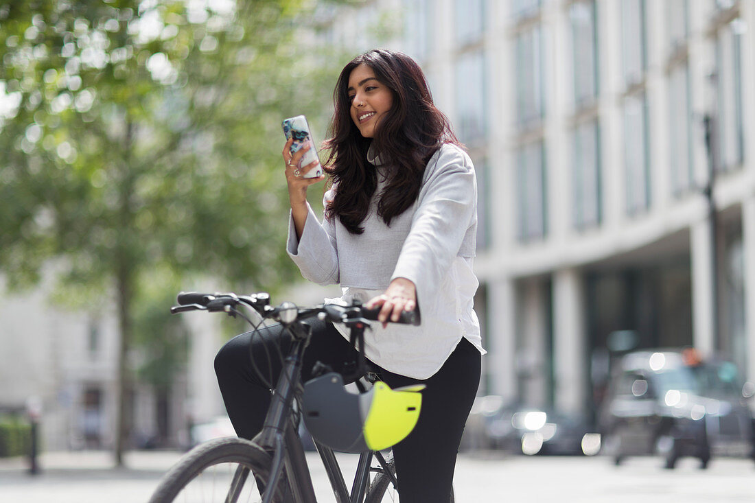 Woman on bicycle using smart phone on city street