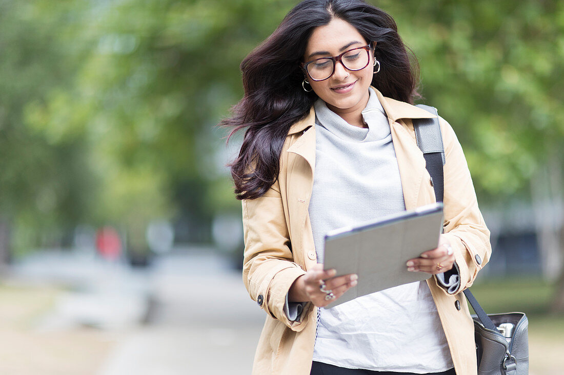 Businesswoman with digital tablet walking in park