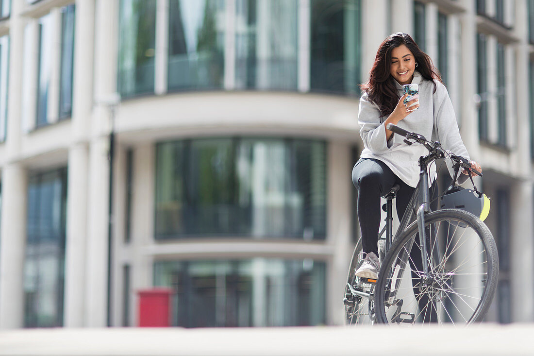 Smiling woman using smart phone on bicycle in city