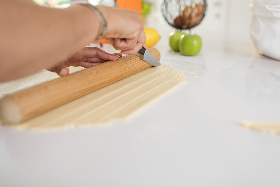 Woman slicing pie dough with knife and rolling pin