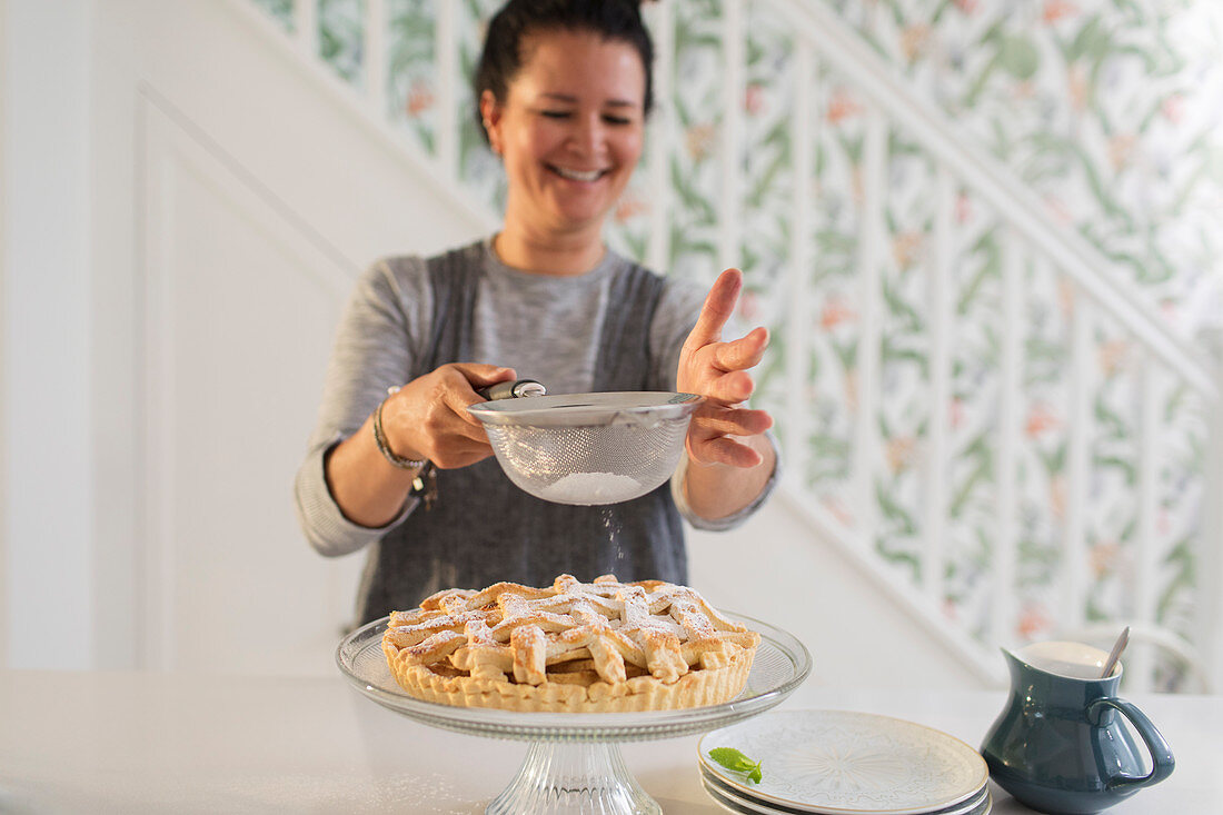 Smiling woman sifting powdered sugar over pie