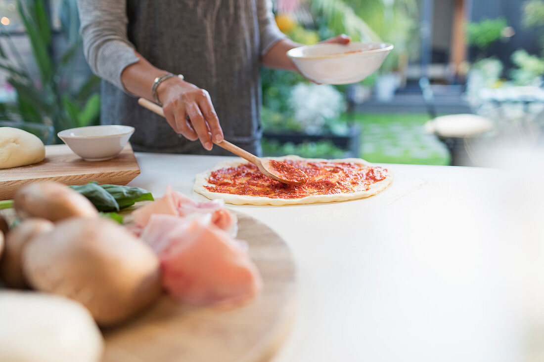 Woman spreading tomato sauce on pizza dough