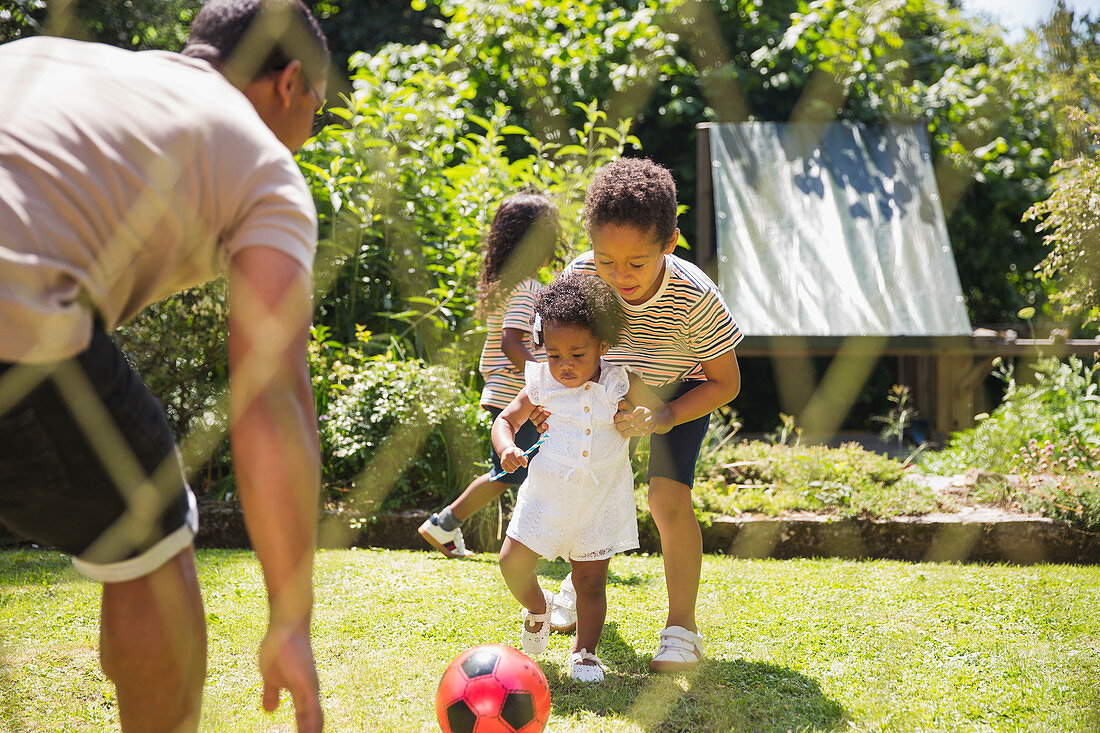 Family playing soccer in sunny summer backyard