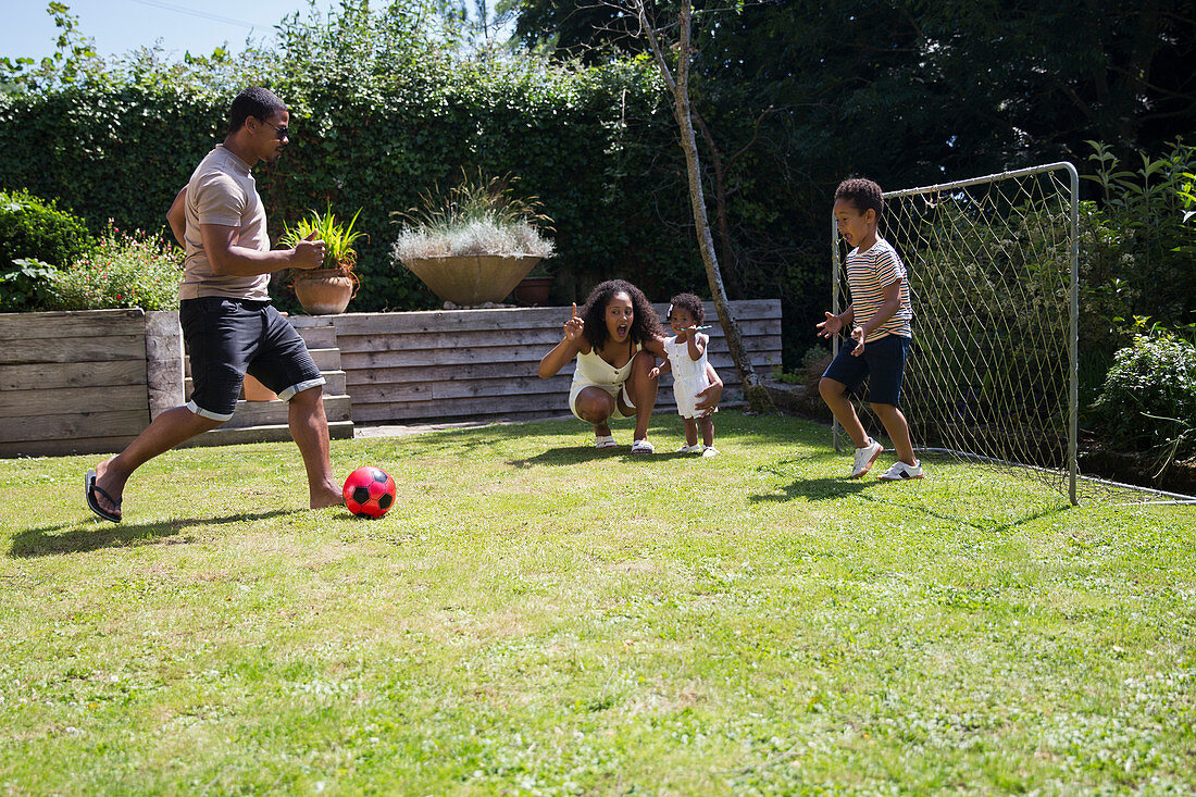 Family playing soccer in sunny summer backyard