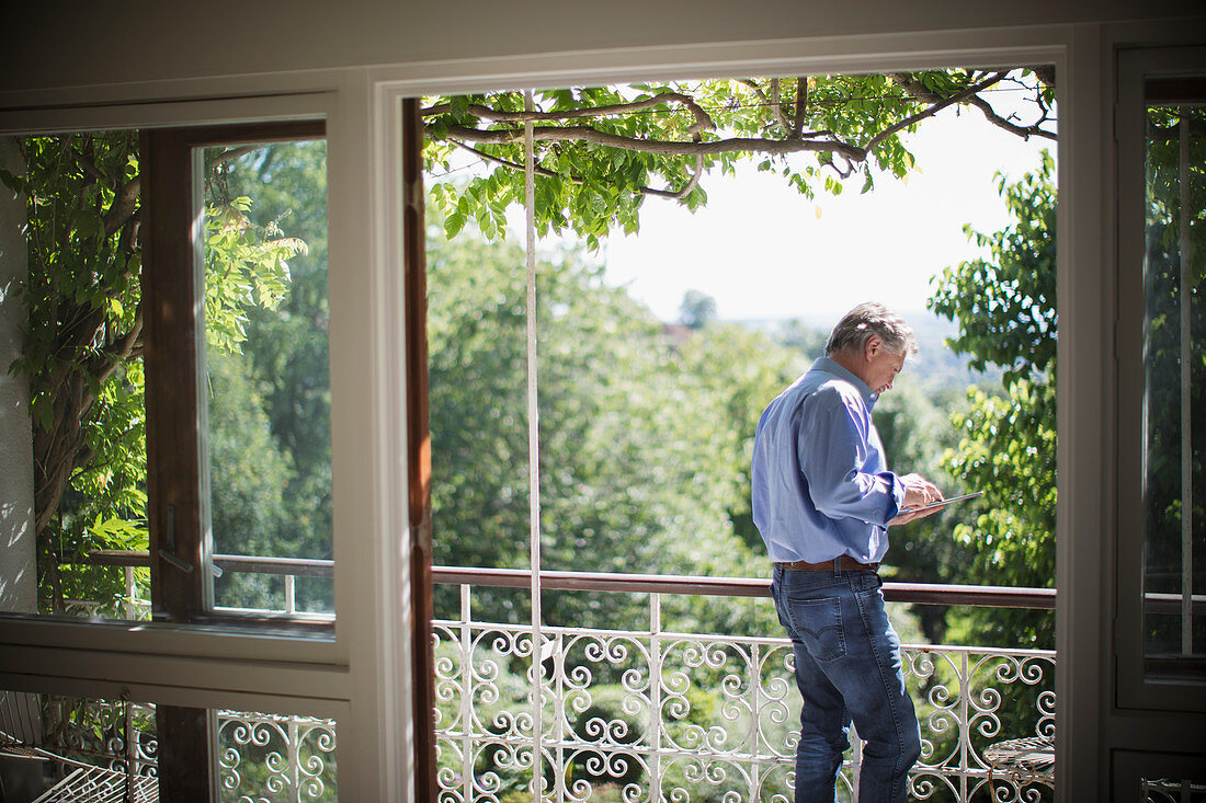 Senior man using tablet on sunny idyllic balcony