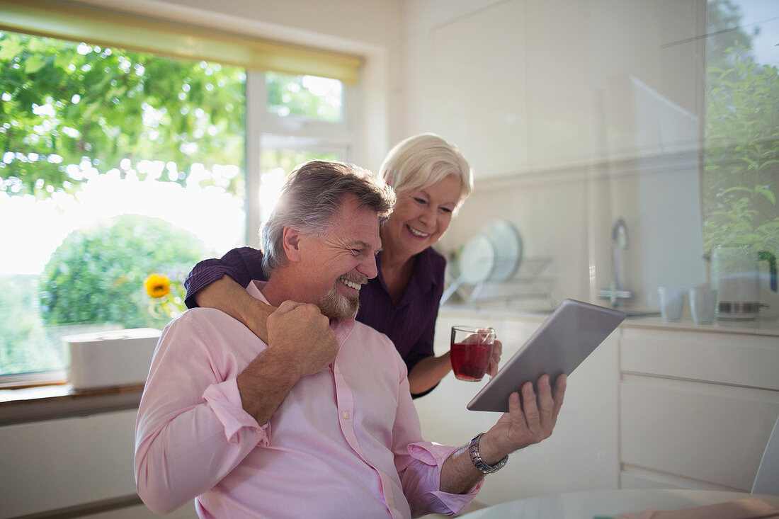 Happy senior couple using tablet in kitchen