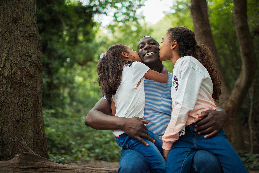 Daughters kissing father below trees