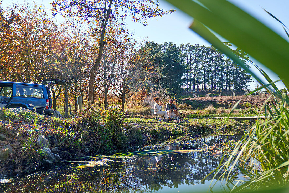 Couple relaxing outside car at autumn riverbank